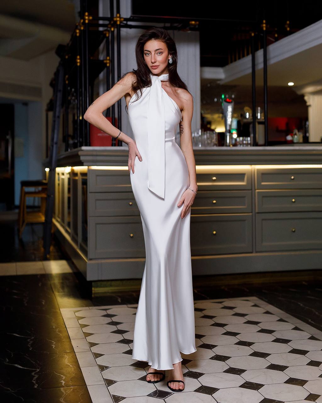 Woman in a white evening gown standing in an elegant interior setting.