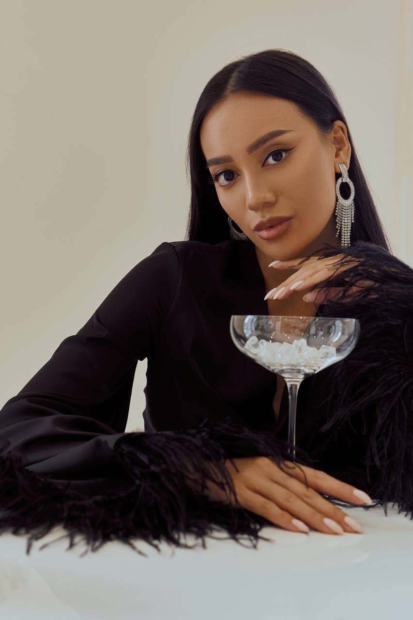 Woman in a black outfit with feathered sleeves holding a martini glass.