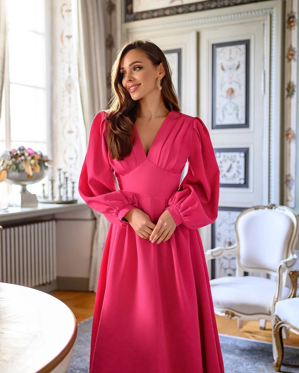 Woman in a pink dress standing in an elegant room with classical decor.