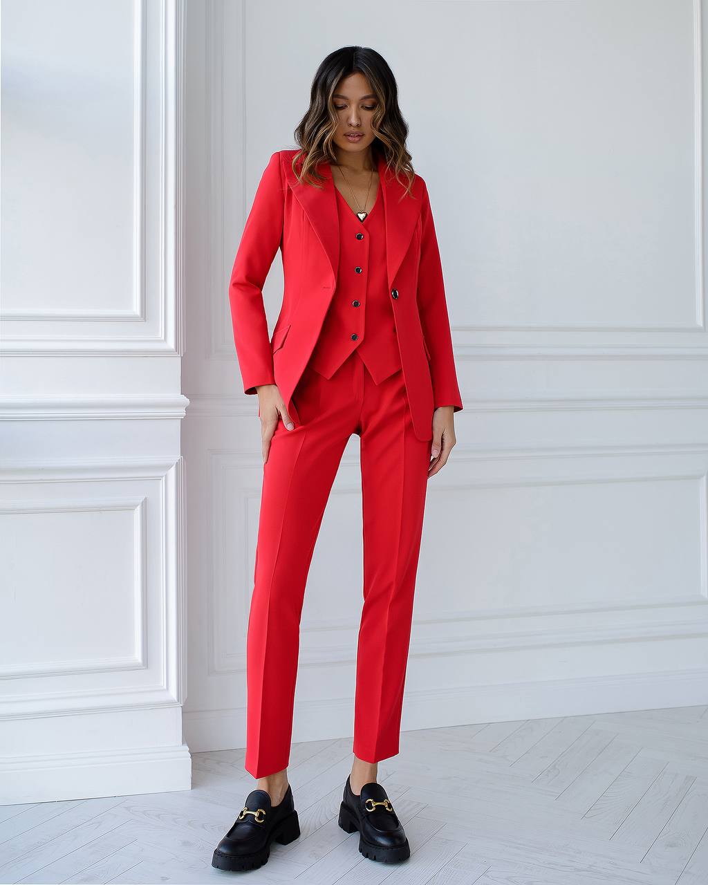 Woman wearing a red suit standing against a white paneled wall.