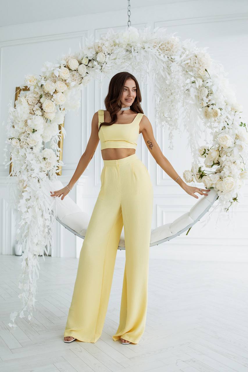 Woman in a yellow outfit standing in front of a floral arch