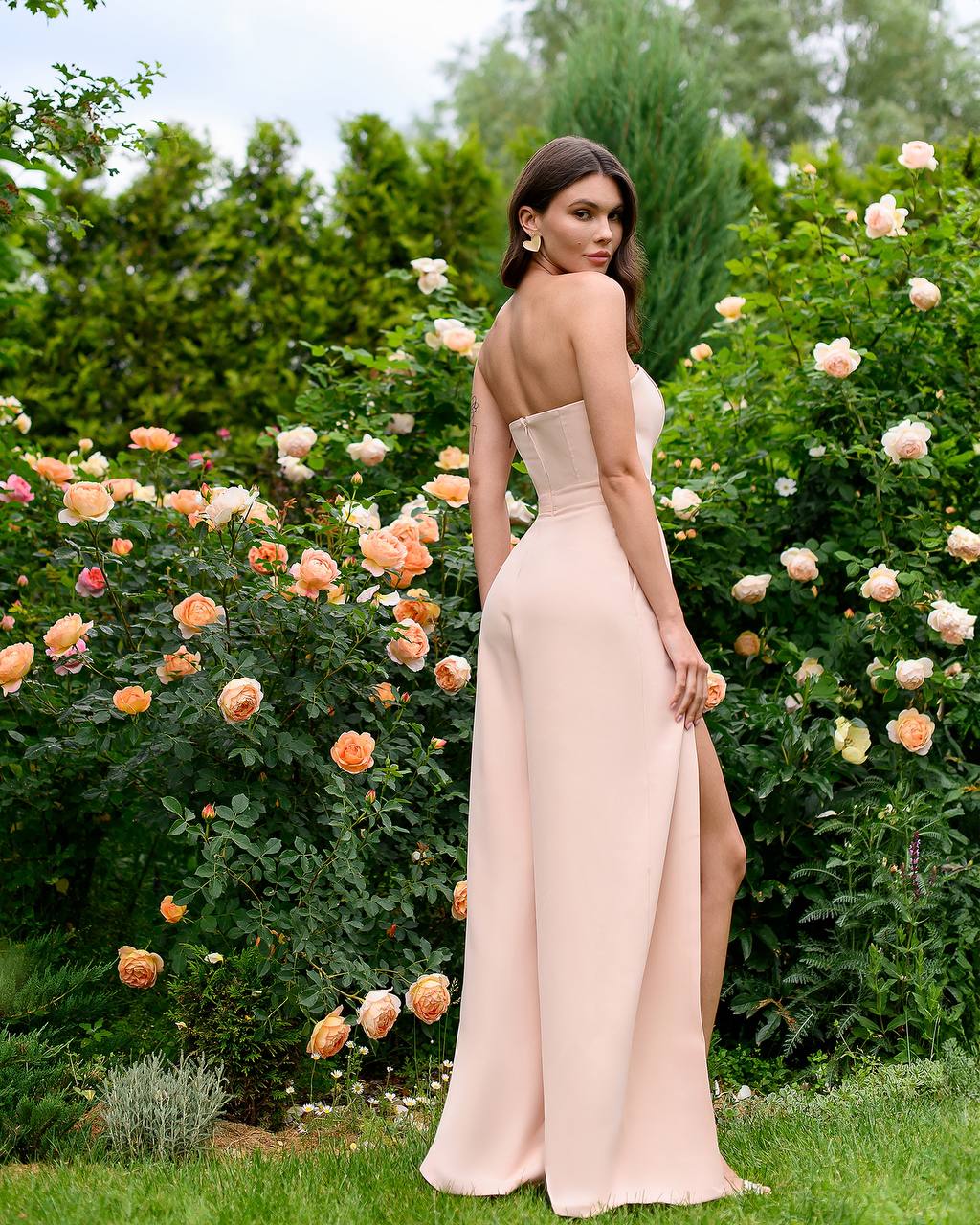 Woman in a long, light-colored dress standing in a garden with flowers