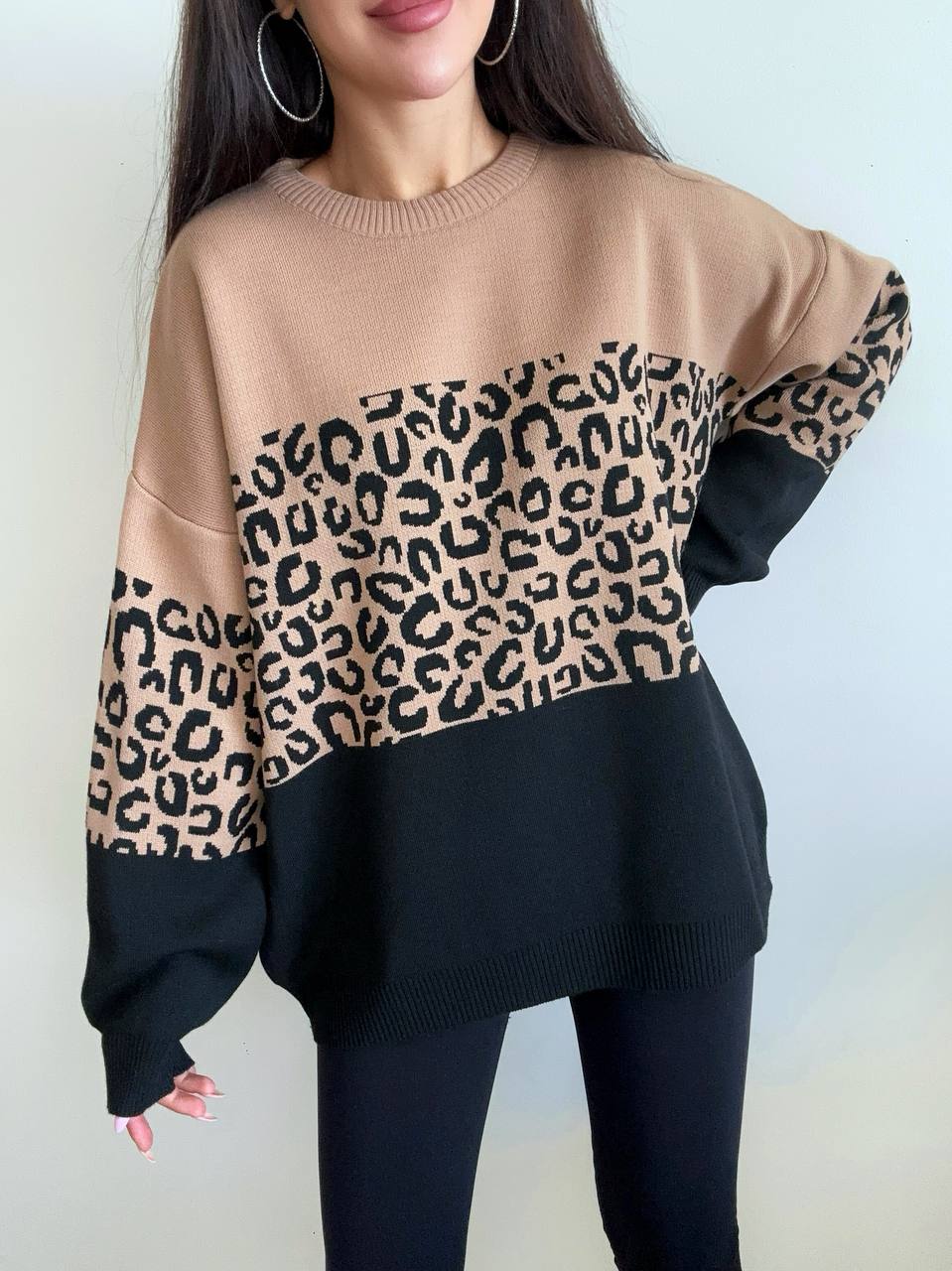 Person wearing a beige and black sweater with leopard print pattern against a white background