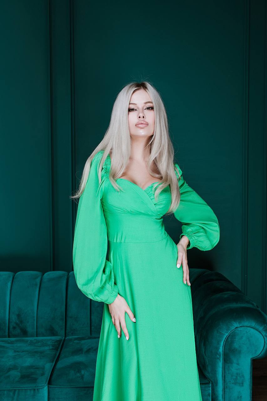 Woman in a green dress standing against a dark teal wall with a green couch.