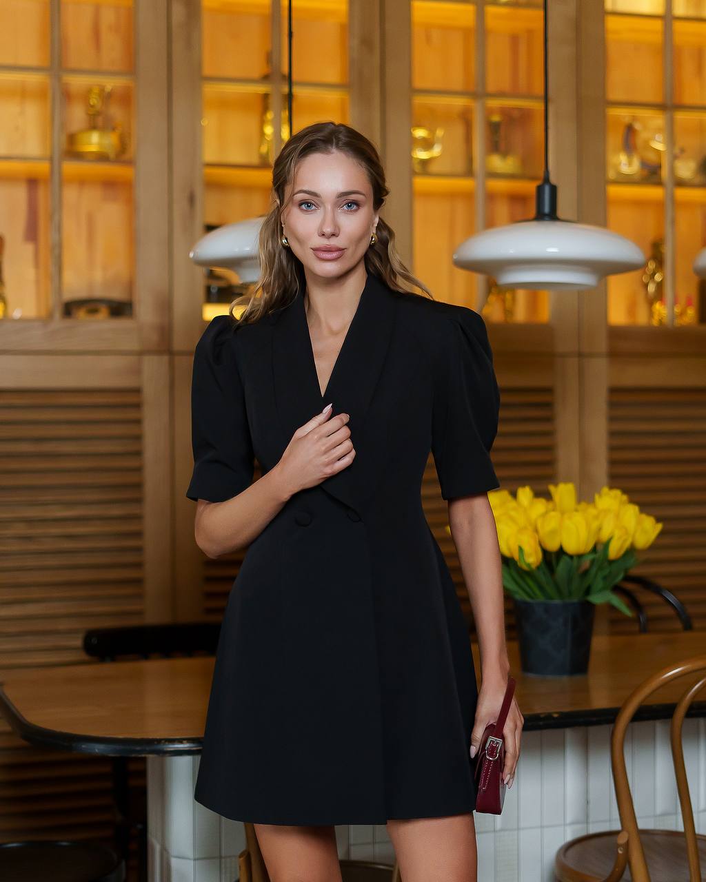 Woman in a black dress standing in a restaurant setting with yellow tulips in the background.
