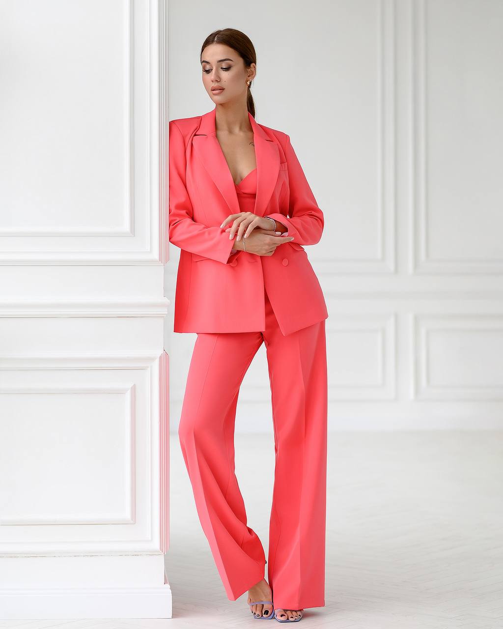 Woman wearing a bright pink suit standing against a white paneled wall.