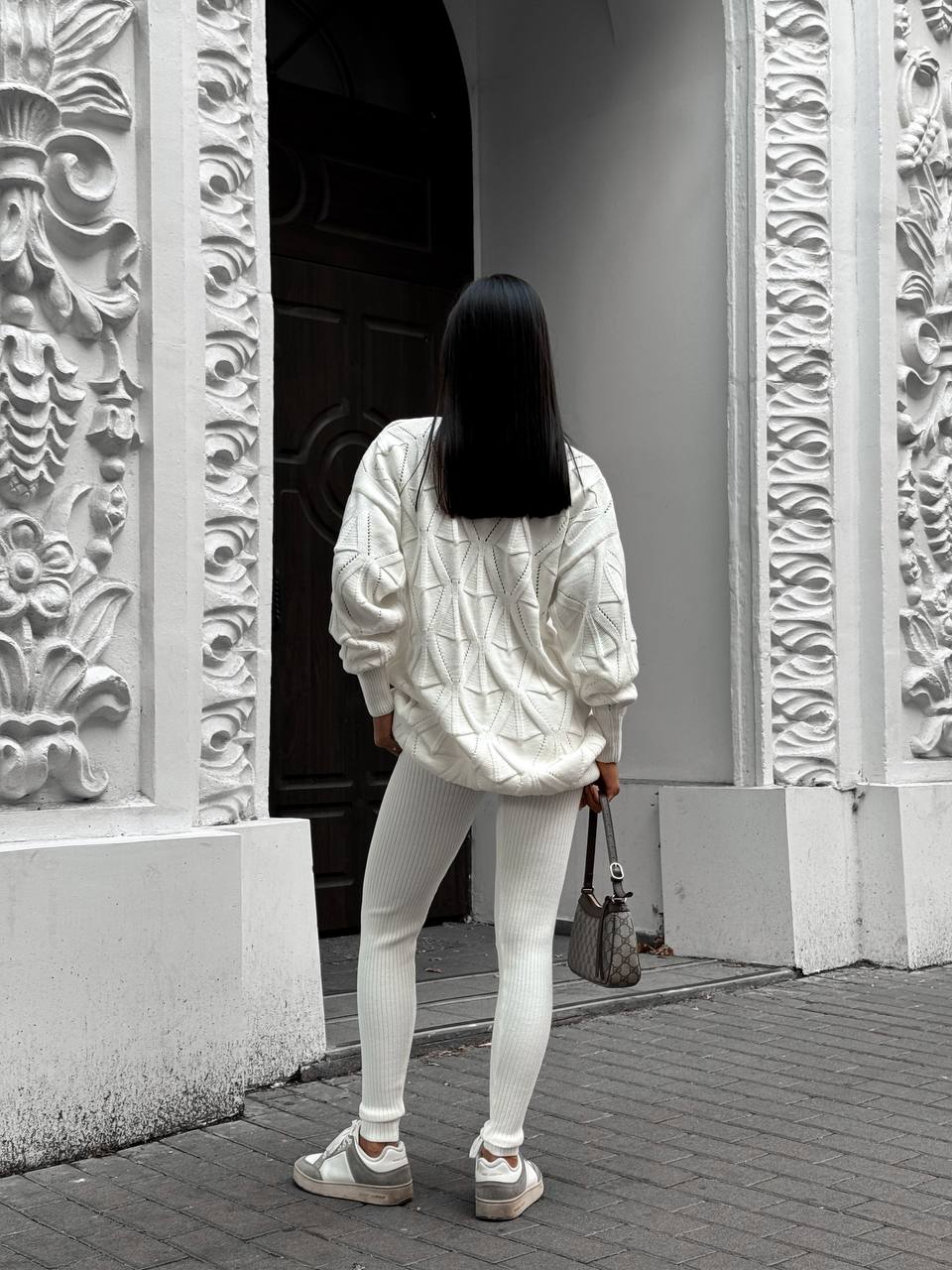 Person wearing a white jacket and pants walking past ornate stone walls.
