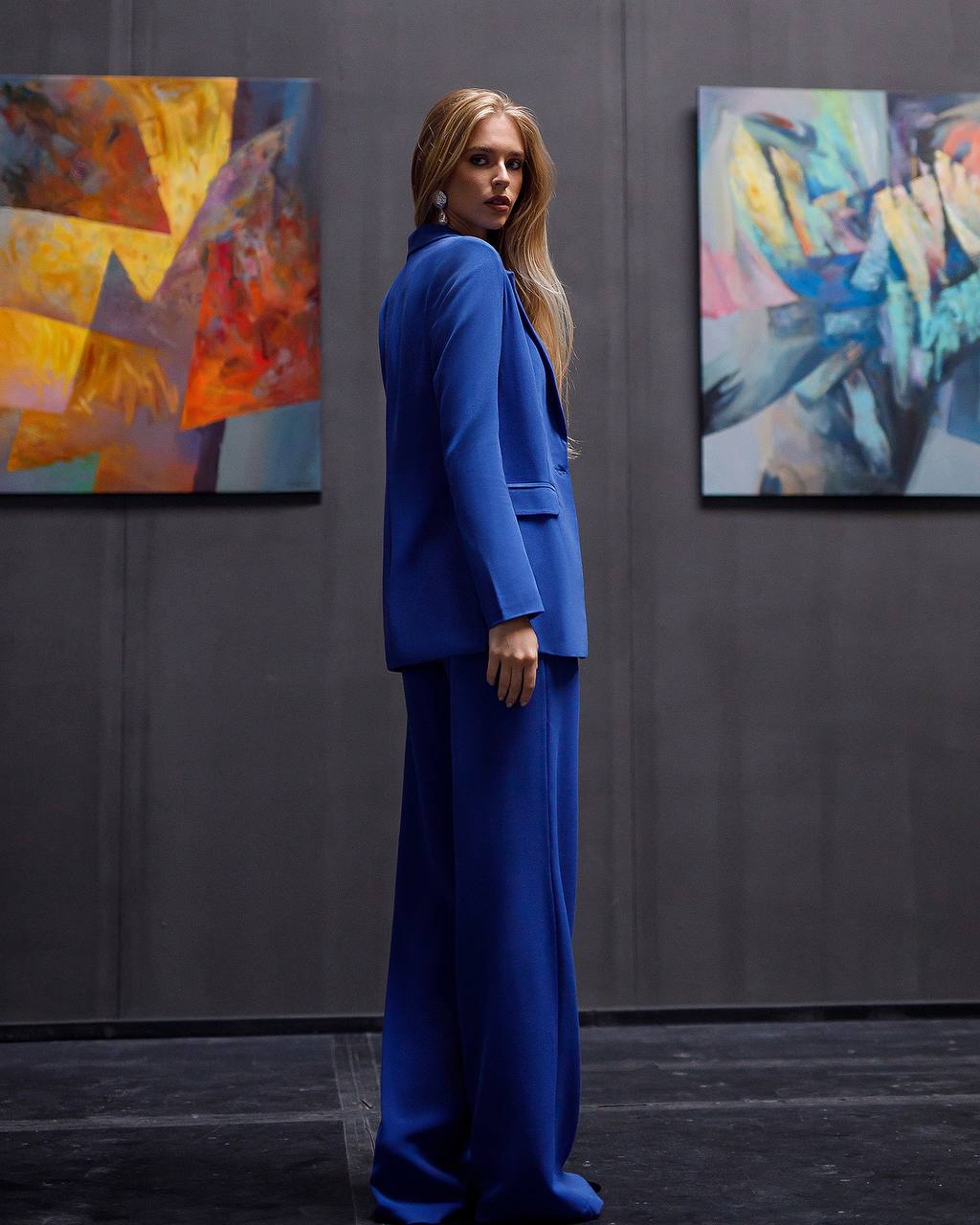 Woman in a blue suit standing in an art gallery with abstract paintings on the wall.
