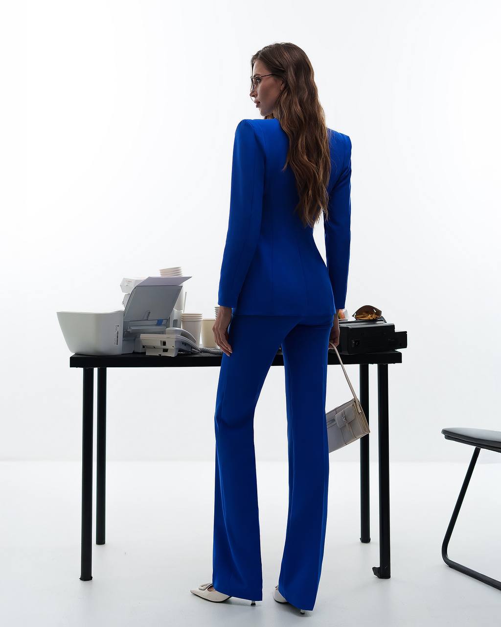 Woman in a blue suit standing at a desk with a white background