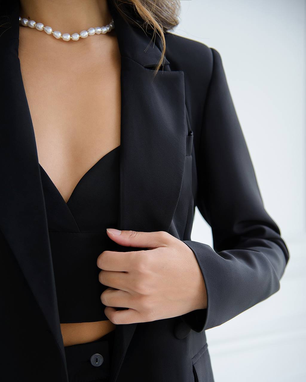 Person wearing a black blazer with a pearl necklace on a light background
