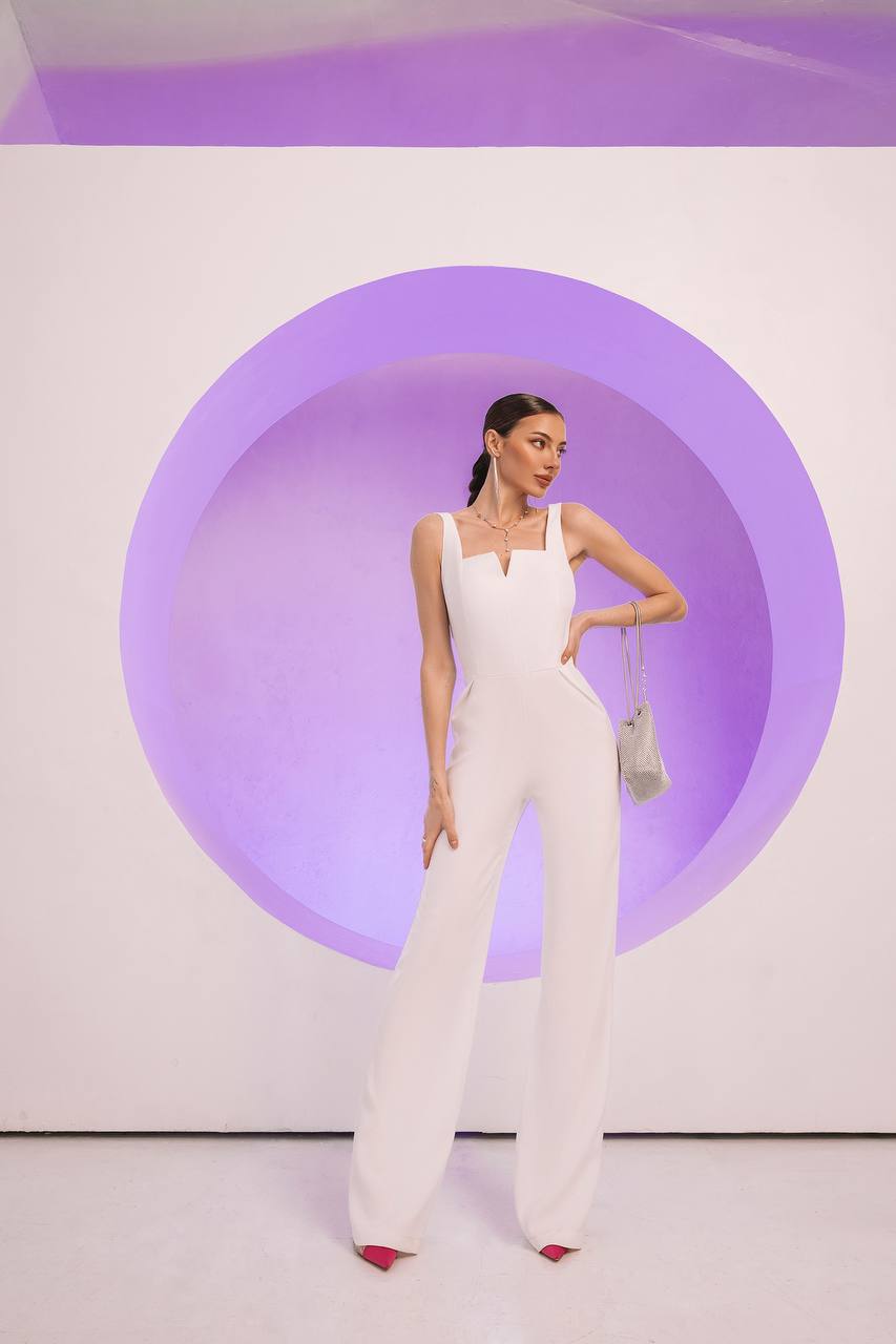 Woman in a white jumpsuit standing against a light purple circular background