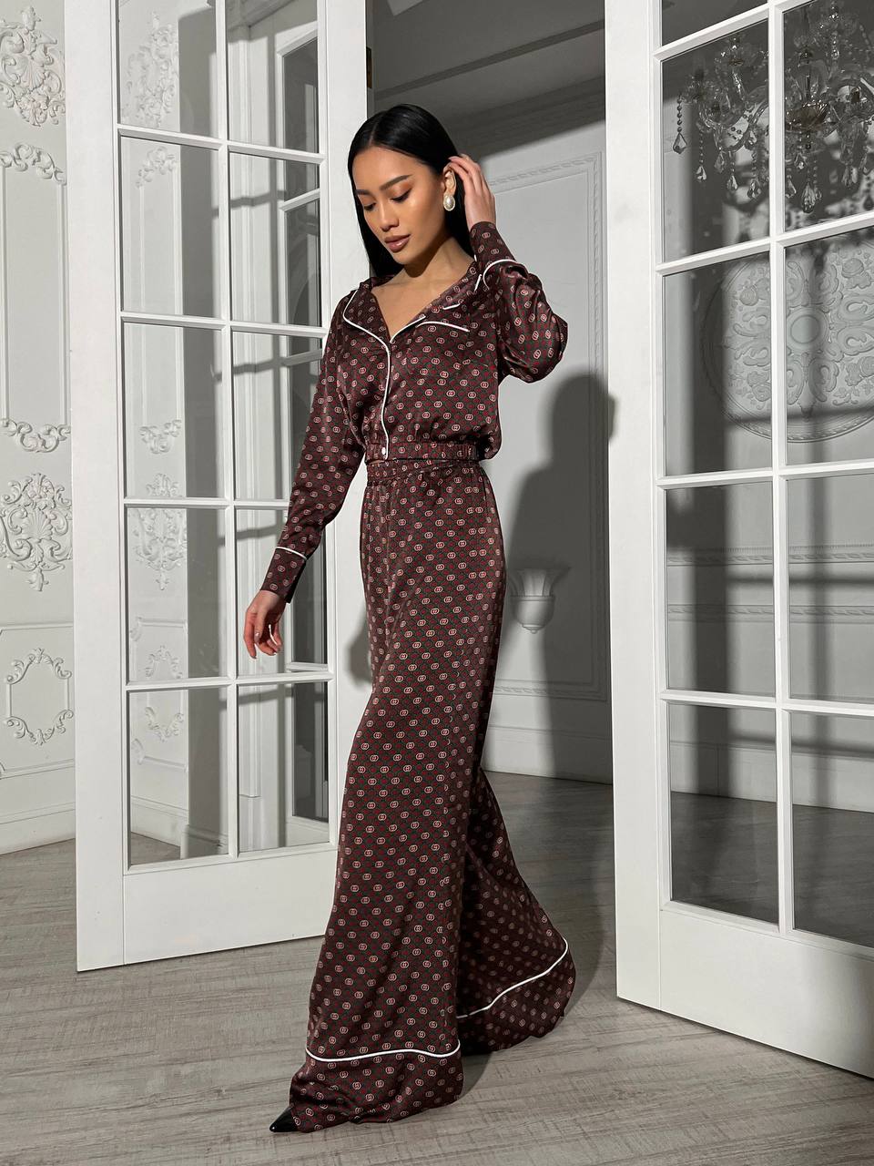 Woman wearing a brown polka dot pajama set standing in a room with white French doors.