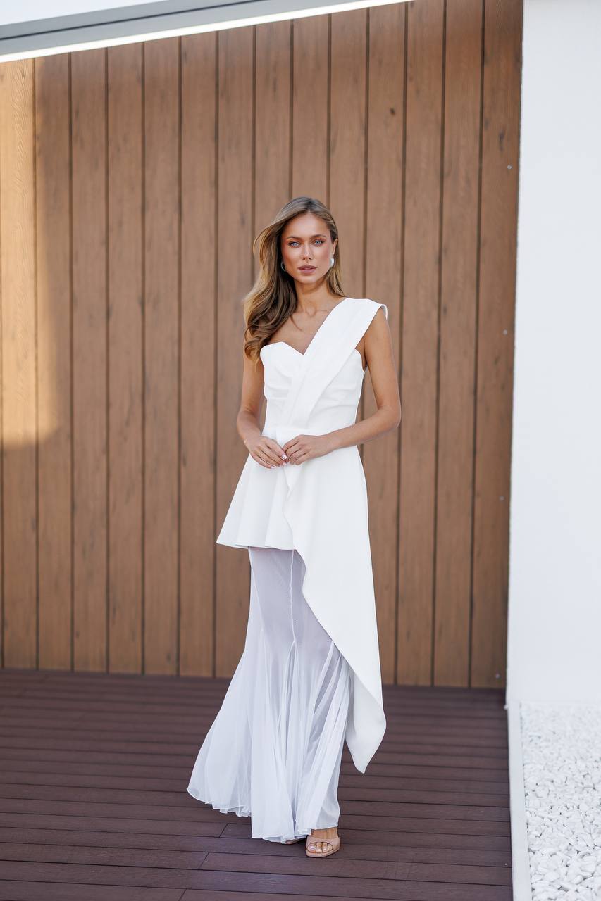Woman in a white dress standing against a wooden wall.