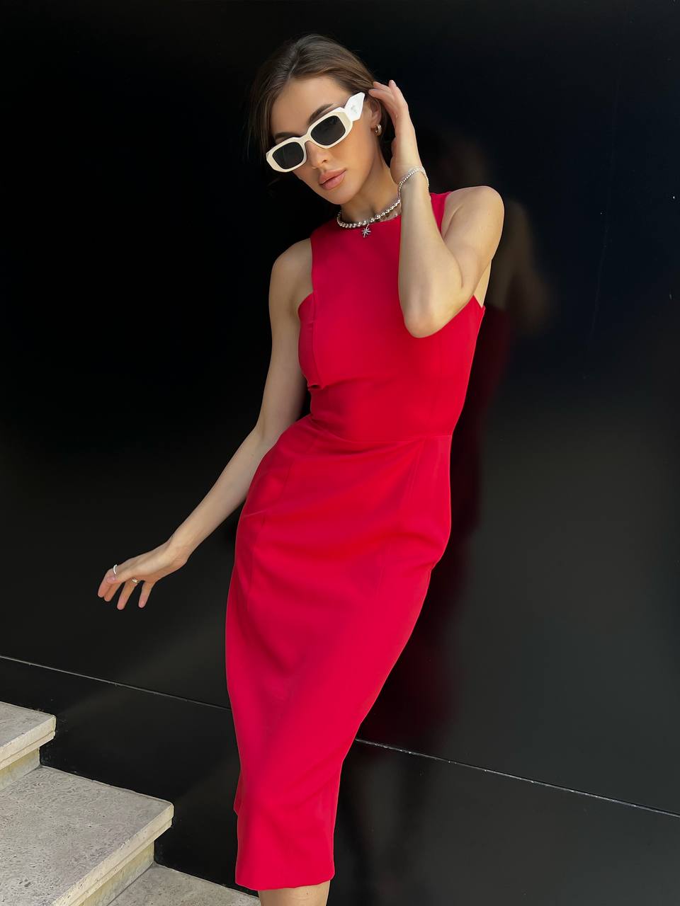 Woman in a red dress and sunglasses posing against a black background