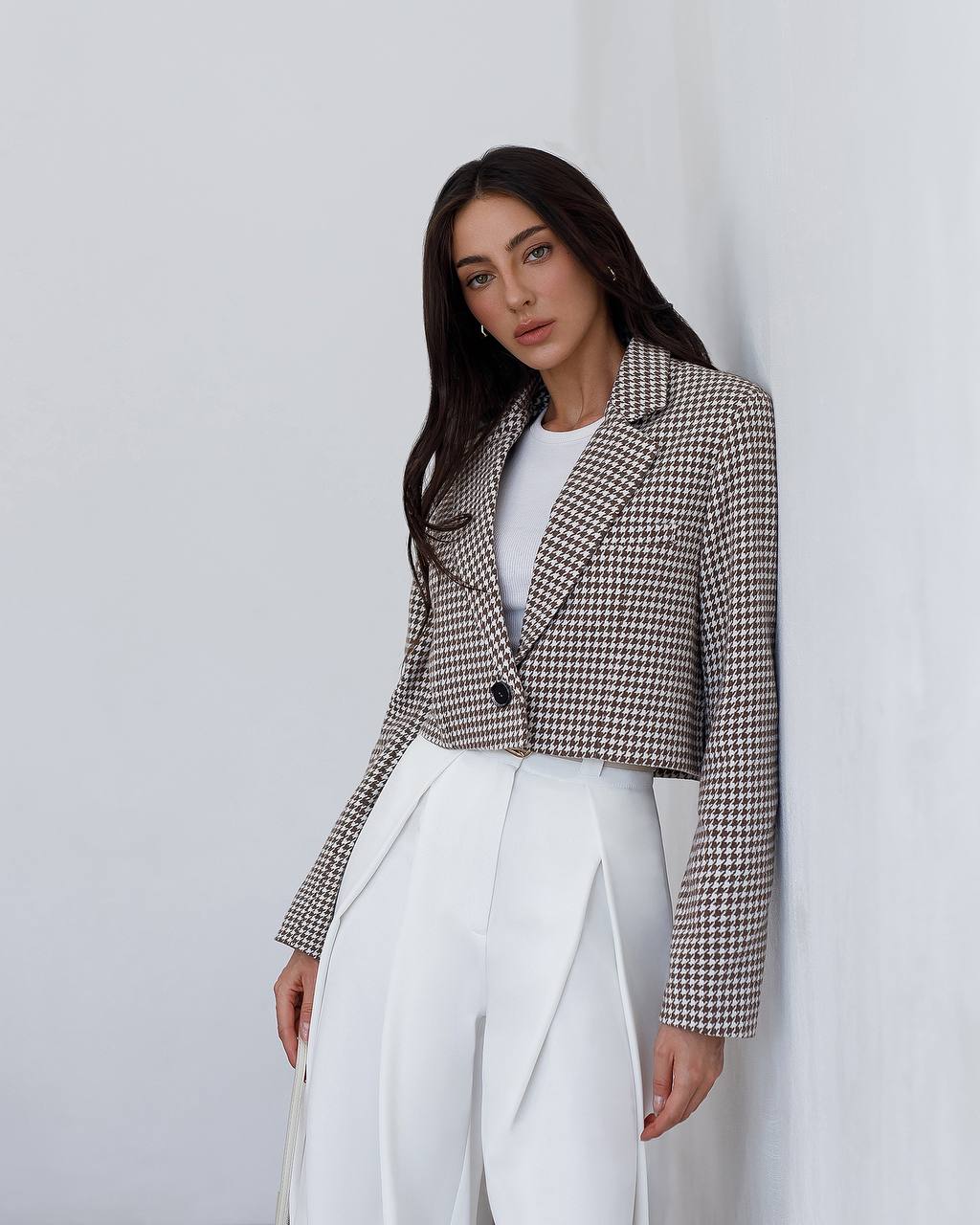 Woman wearing a checkered blazer and white pants against a plain background