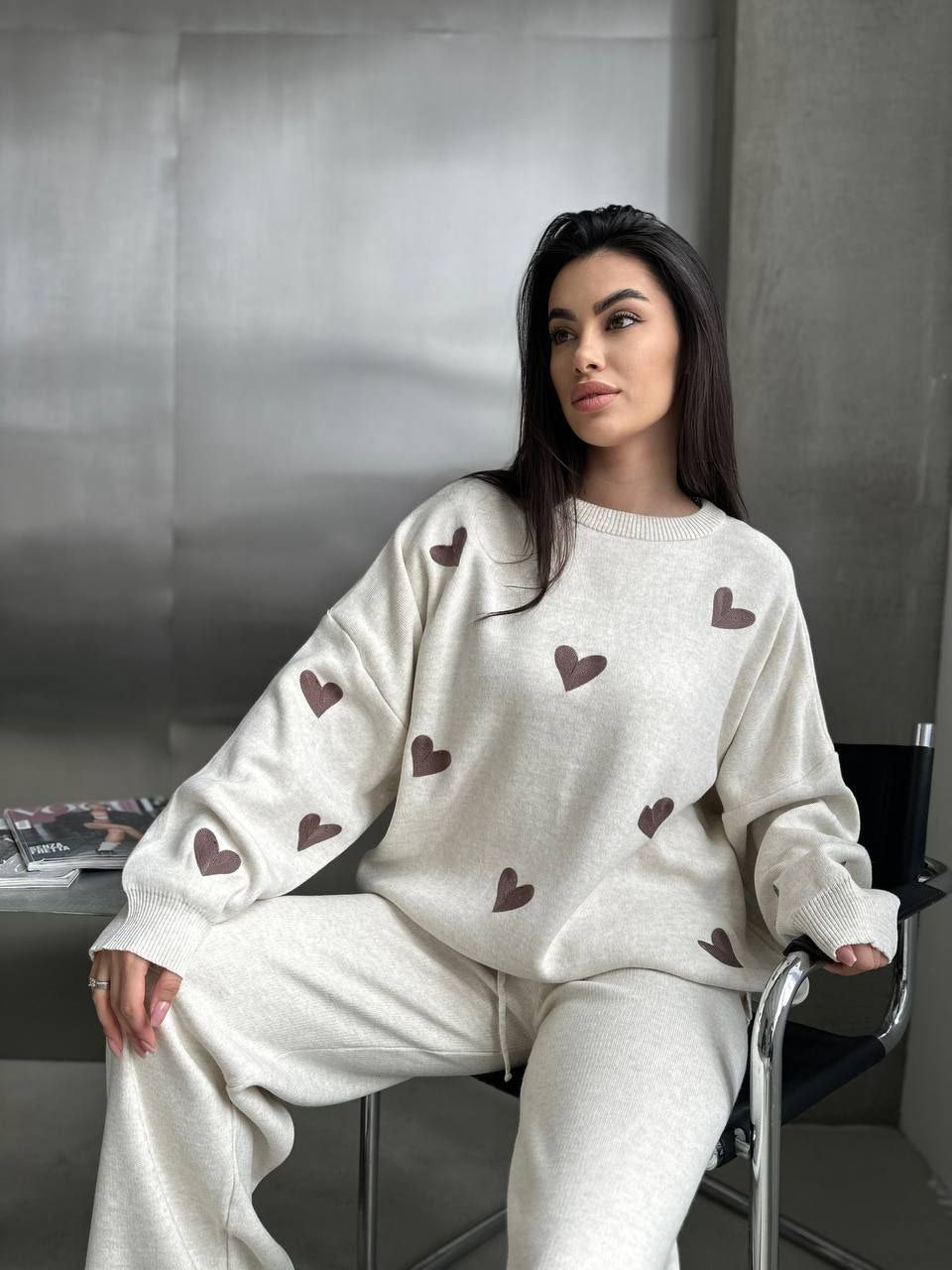 Woman wearing a white sweater with brown heart patterns sitting in an office chair.