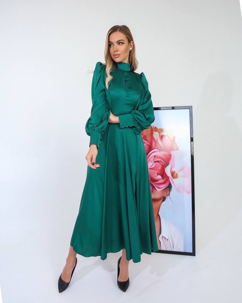 Woman wearing a green dress standing in front of a white wall with a decorative piece.