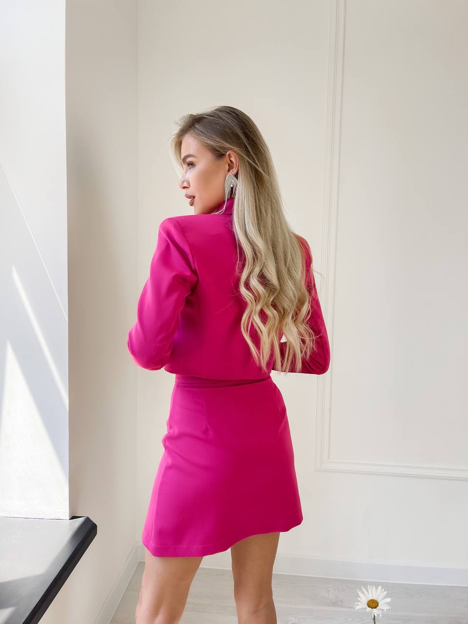Woman wearing a bright pink outfit standing in a minimalistic room.