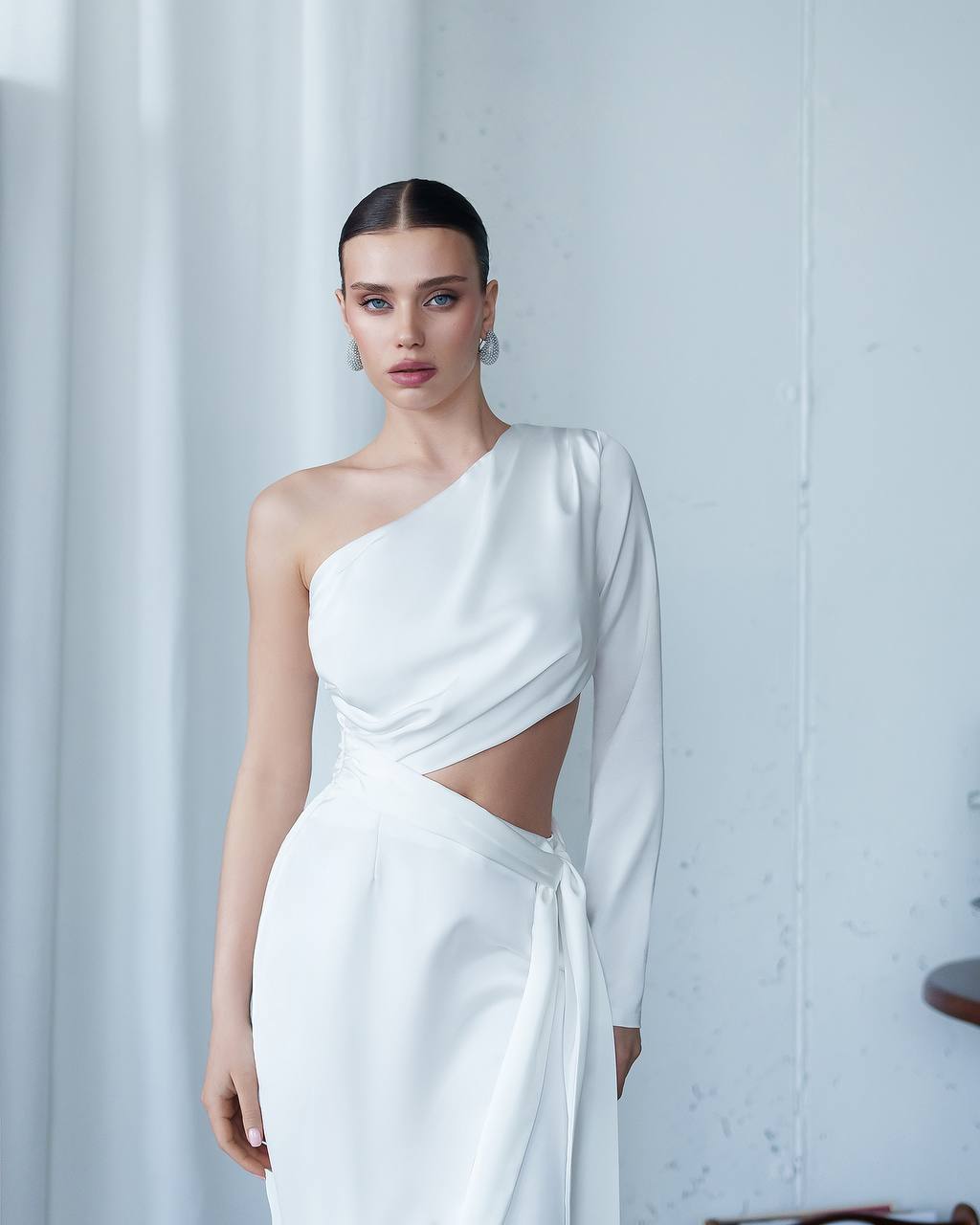 Woman wearing a white one-shoulder dress with a cutout design against a white background