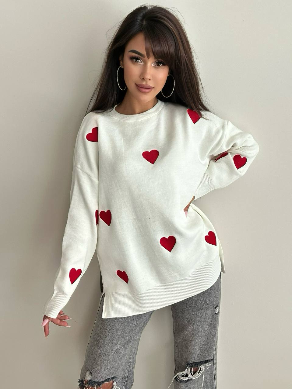 Woman wearing a white sweater with red heart patterns on a plain background