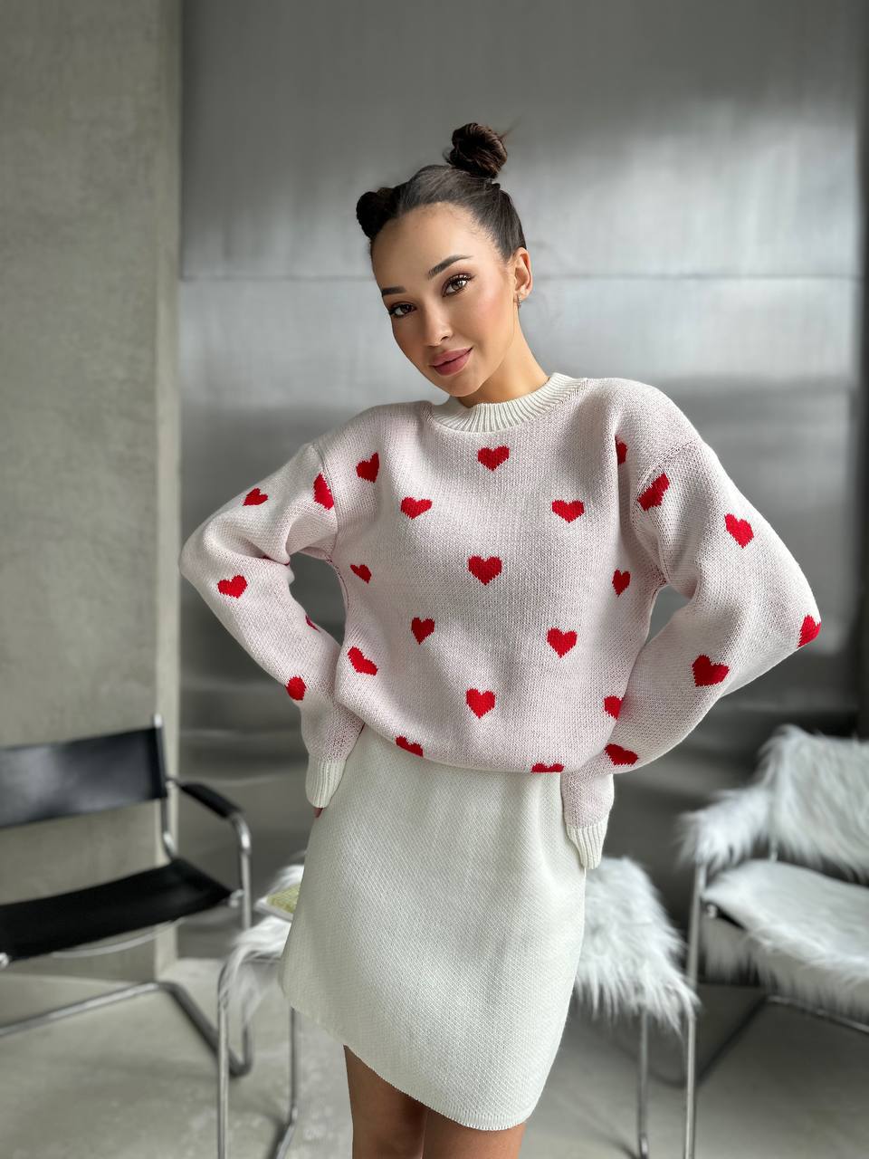 Woman wearing a white sweater with red heart patterns in an indoor setting
