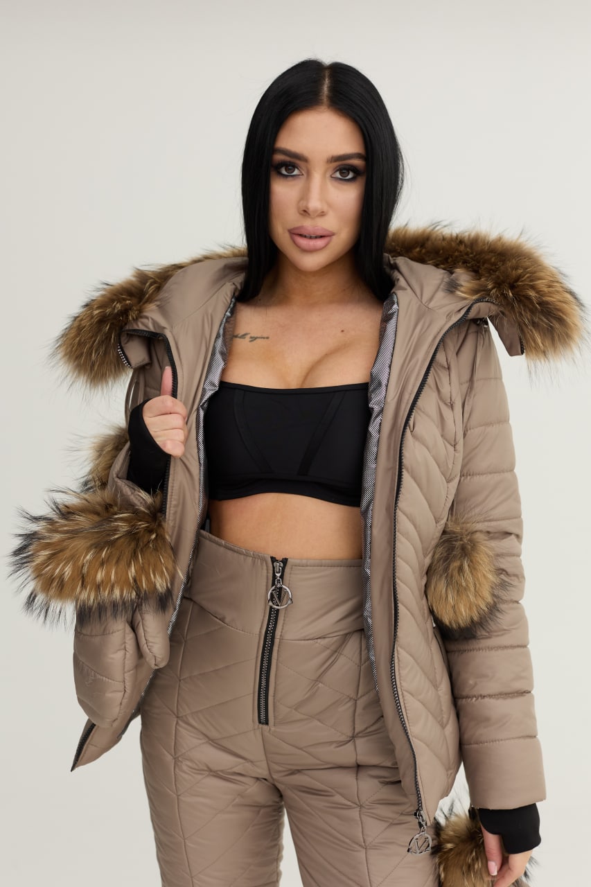 Woman wearing a beige puffer jacket with fur trim on a plain background
