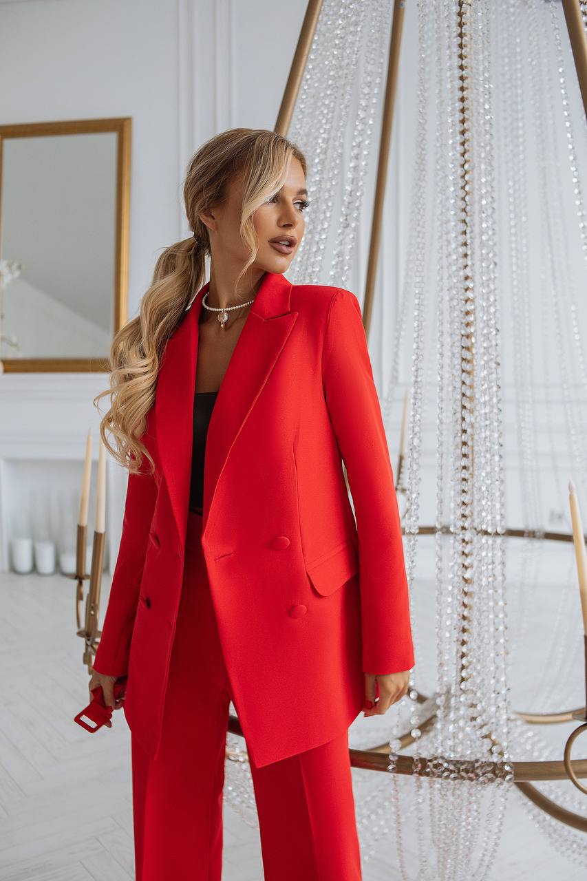 Woman in a red suit standing in a stylish interior setting with decorative elements.