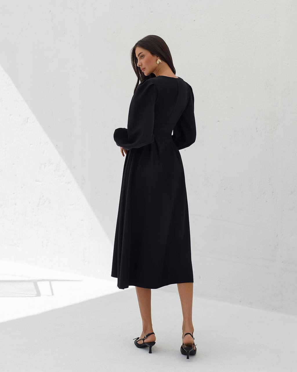 Woman wearing a black dress standing in a minimalistic white room