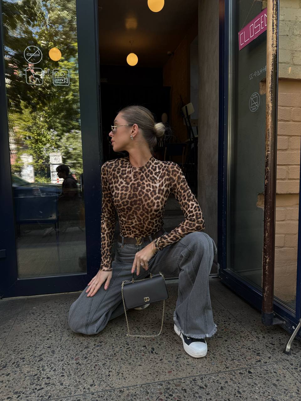 Woman in leopard print top and gray pants sitting outside a store.
