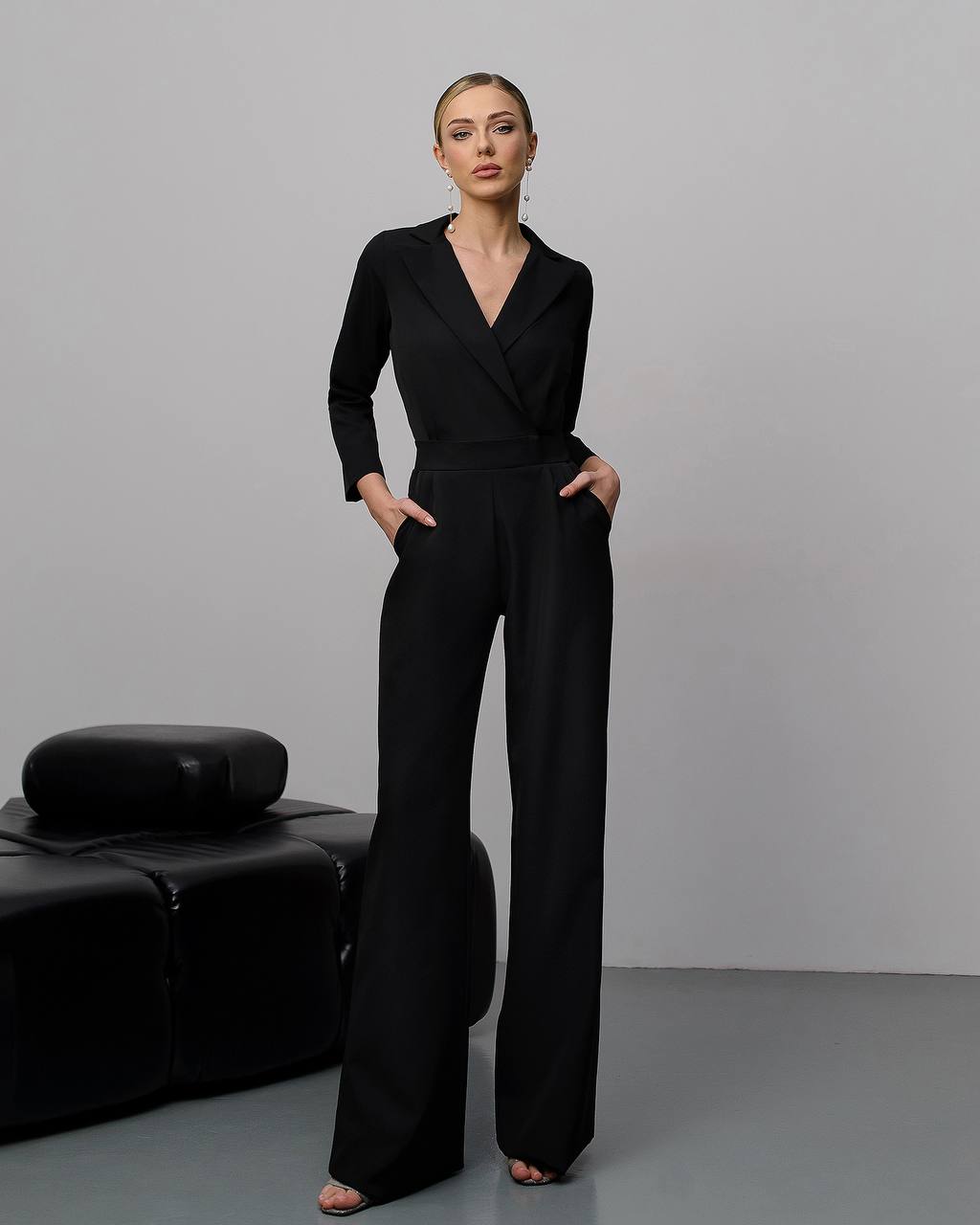 Woman wearing a black jumpsuit standing against a plain background