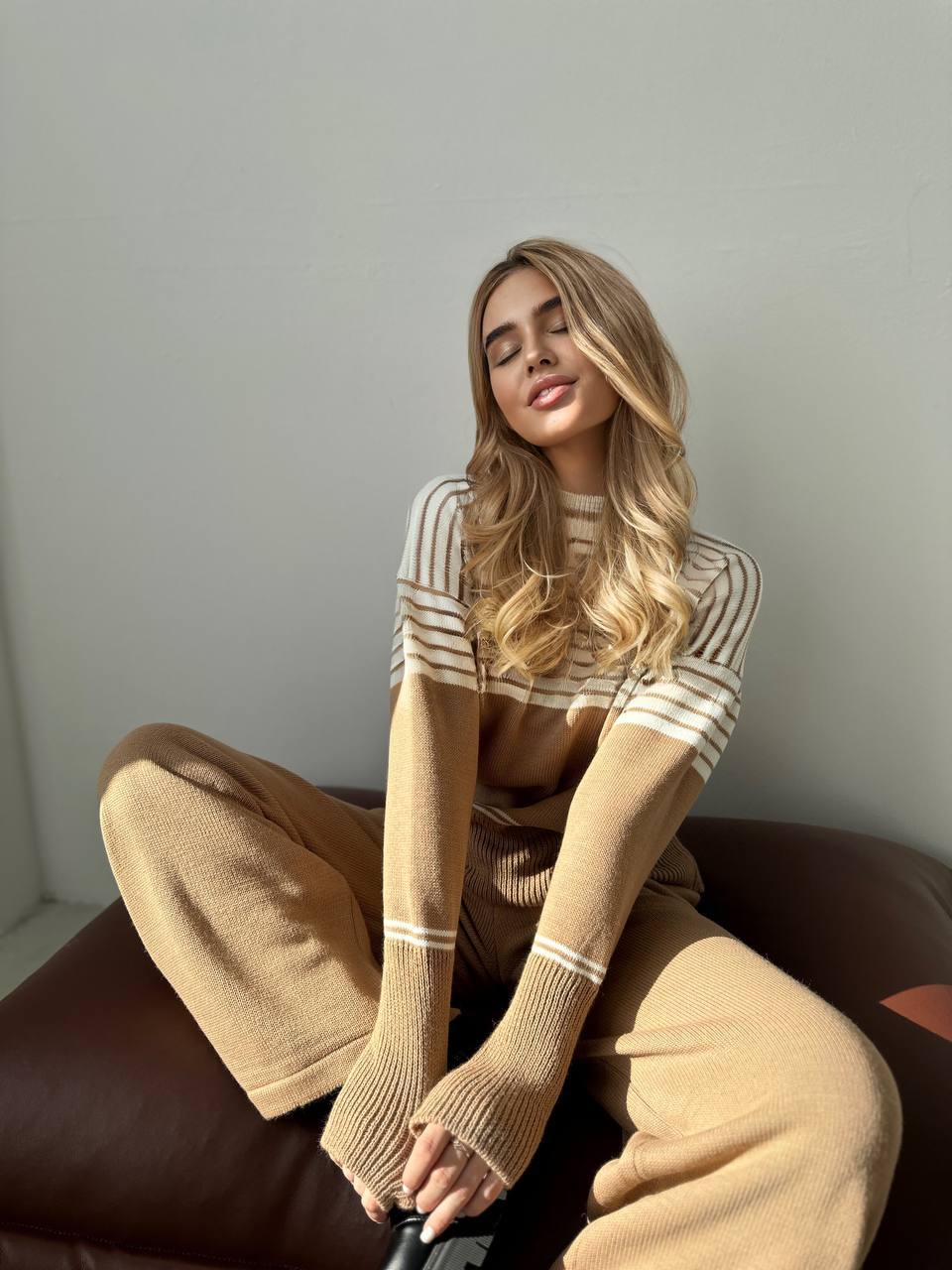 Woman wearing a beige and white striped sweater sitting on a brown chair.