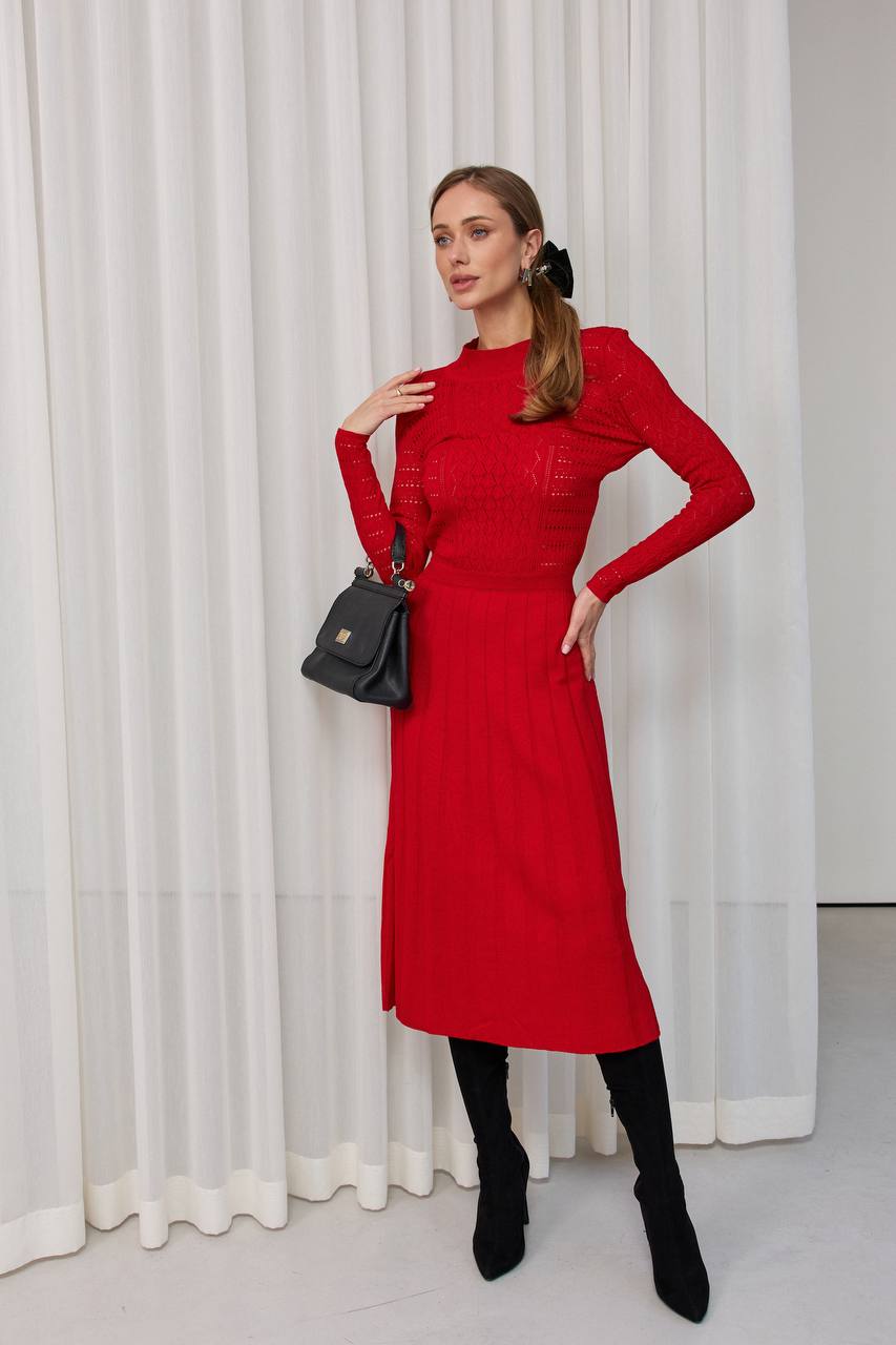 Woman wearing a red dress with long sleeves against a white curtain background