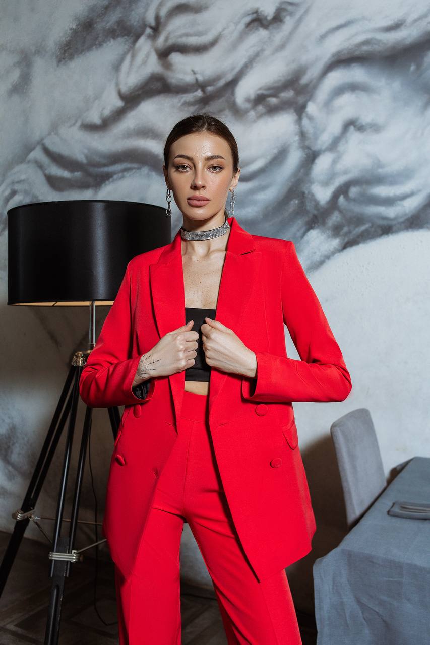 Woman in a red suit standing in a room with a textured wall and lamp.