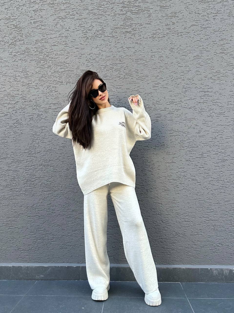 Woman in a white outfit posing against a gray wall