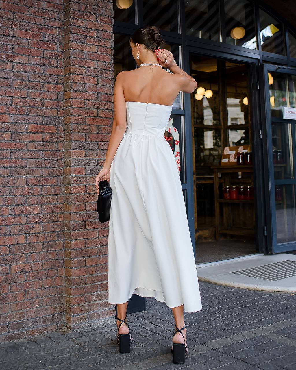 Woman in a white strapless dress standing against a brick wall.