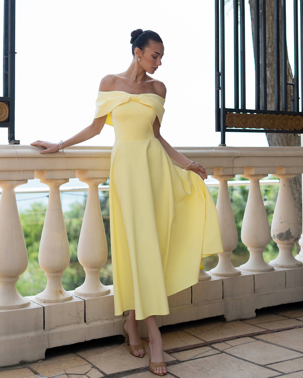 Woman in a yellow off-shoulder dress standing on a balcony.