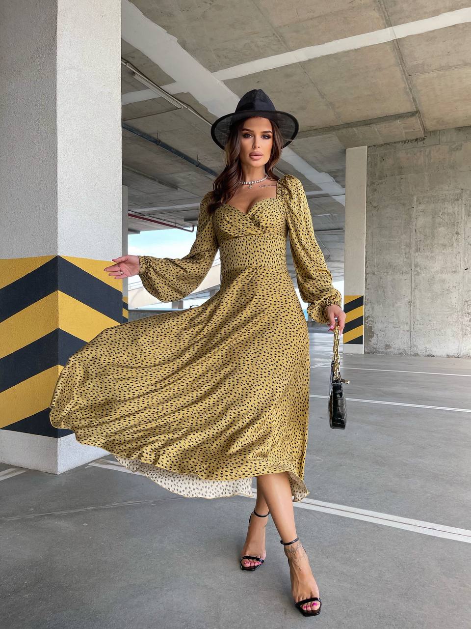 Woman in a yellow dress and black hat posing in an urban setting.