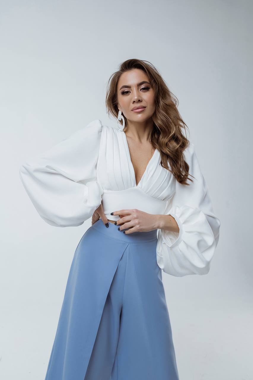 Woman wearing a white blouse with wide sleeves and light blue pants on a white background