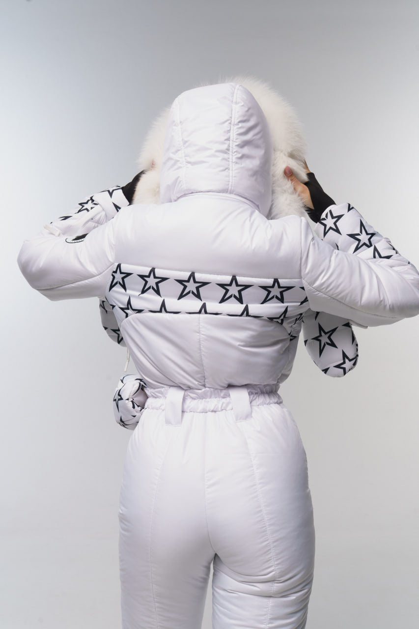 Person wearing a white puffer jacket with star patterns and white pants on a light gray background