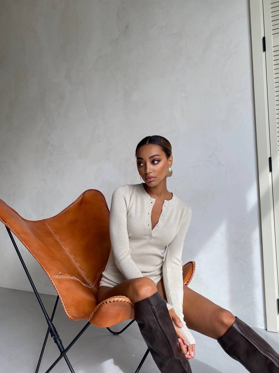 Woman sitting on a brown leather chair wearing a white outfit and brown knee-high boots.