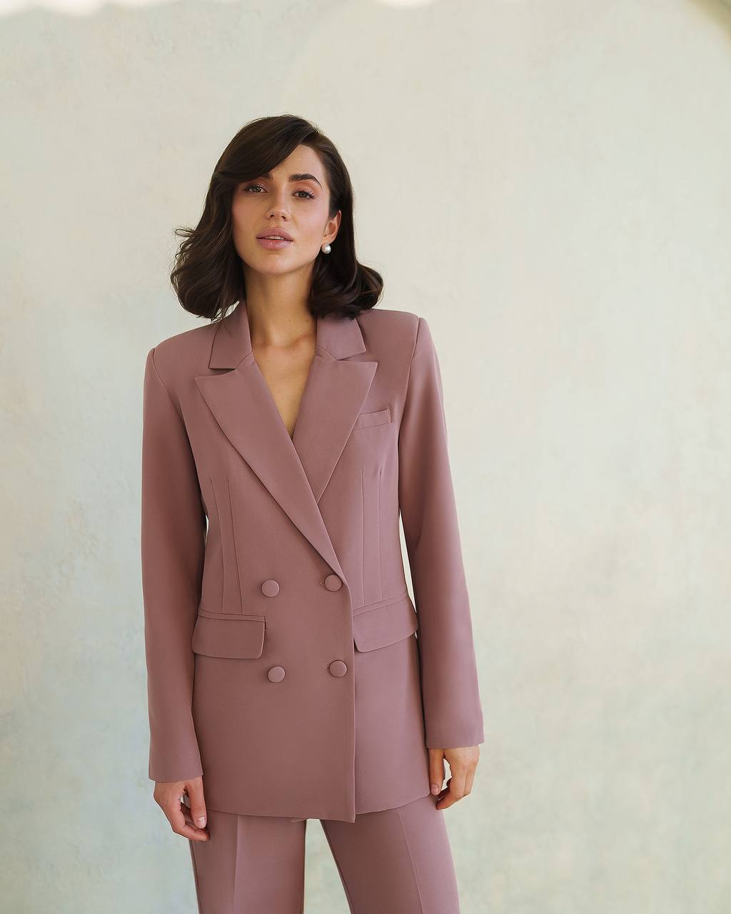 Woman wearing a mauve suit against a plain background