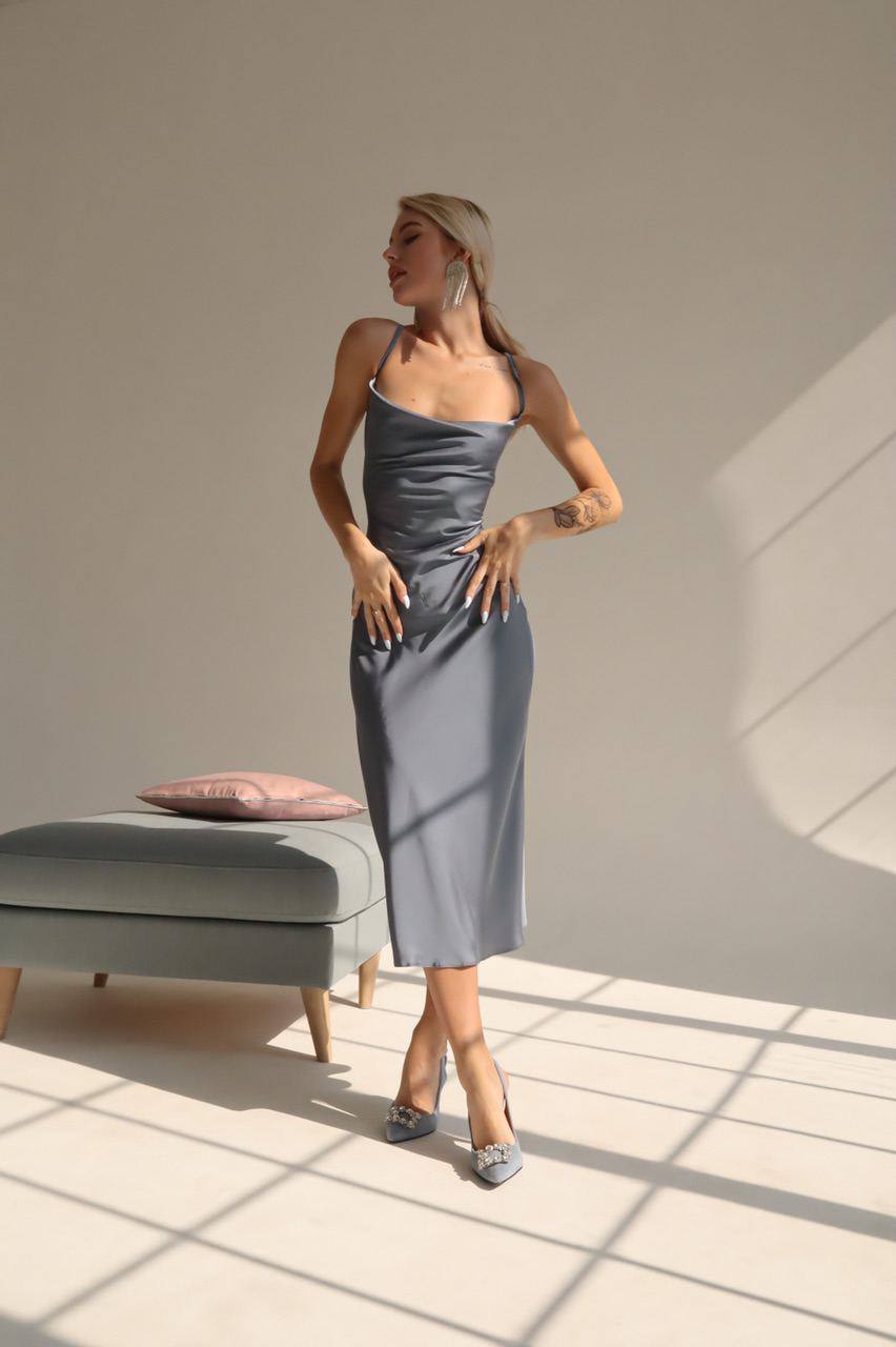 Woman in a gray dress standing in a sunlit room with a neutral background