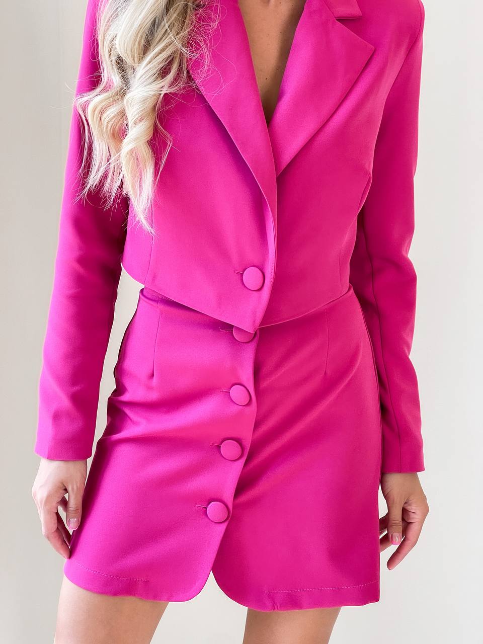 Person wearing a bright pink suit with a matching dress on a plain background