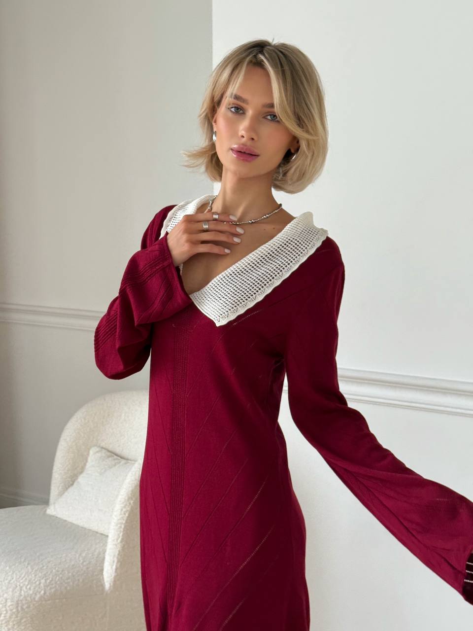 Woman wearing a burgundy dress with white trim in an elegant room.