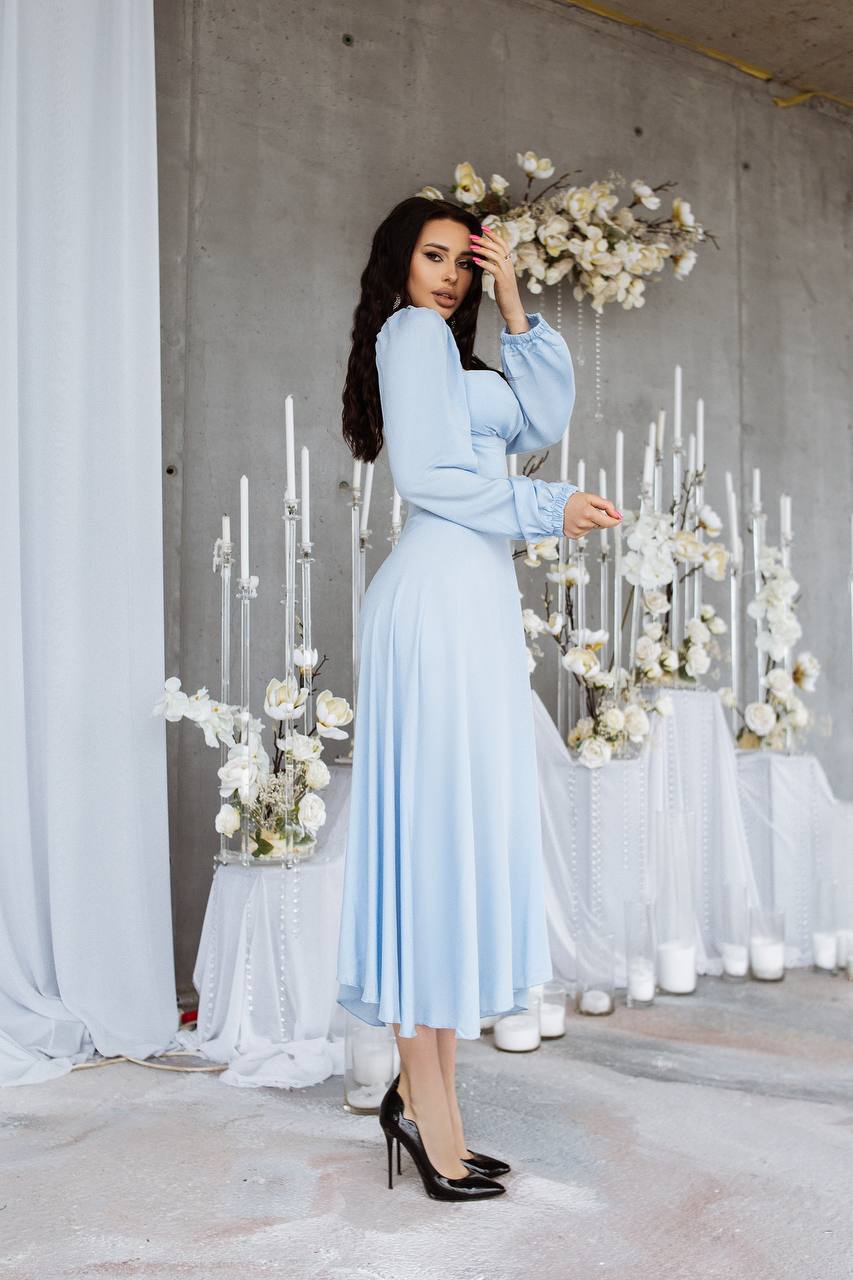 Woman in a light blue dress standing in front of a decorative setup with flowers and candles.
