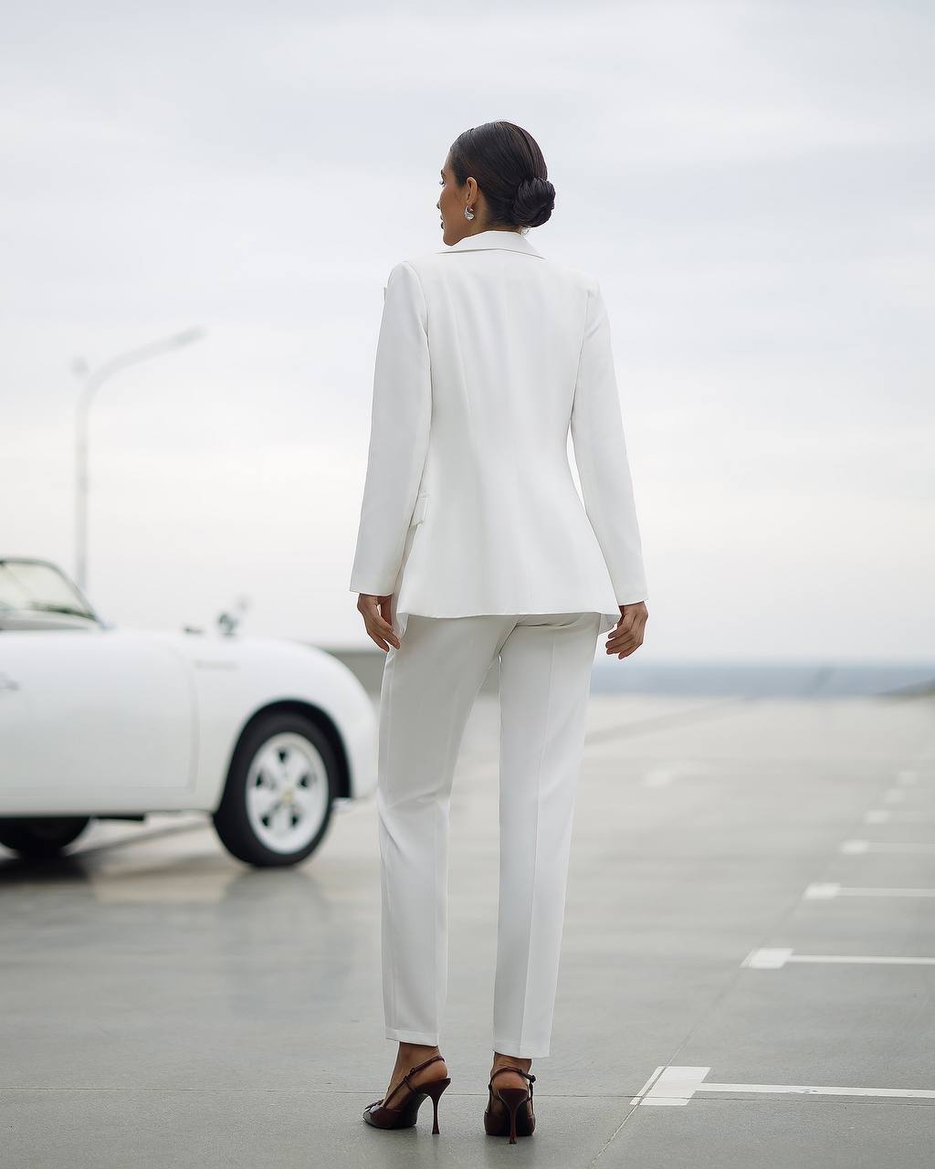 Person wearing a white suit standing on a road with a car in the background