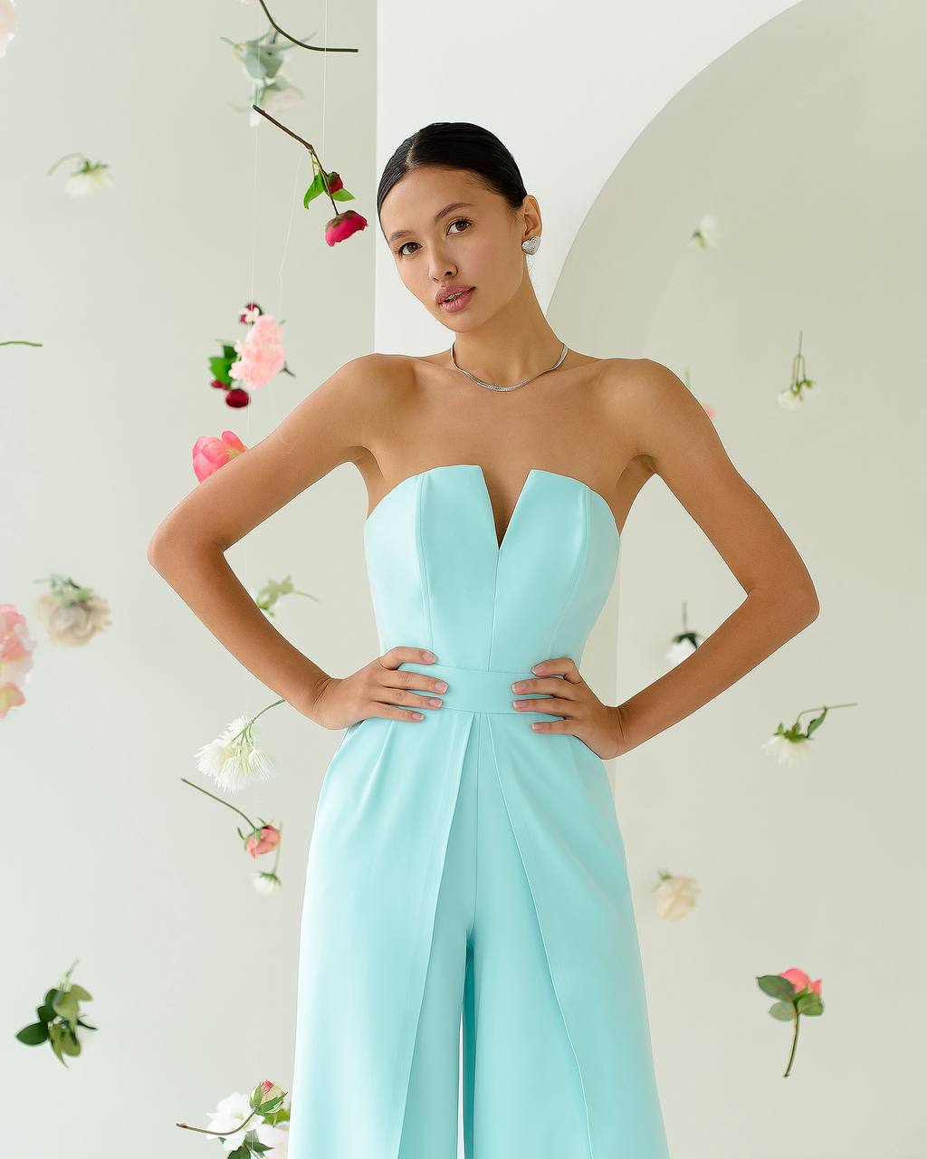 Woman wearing a strapless light blue gown against a floral decorated wall.