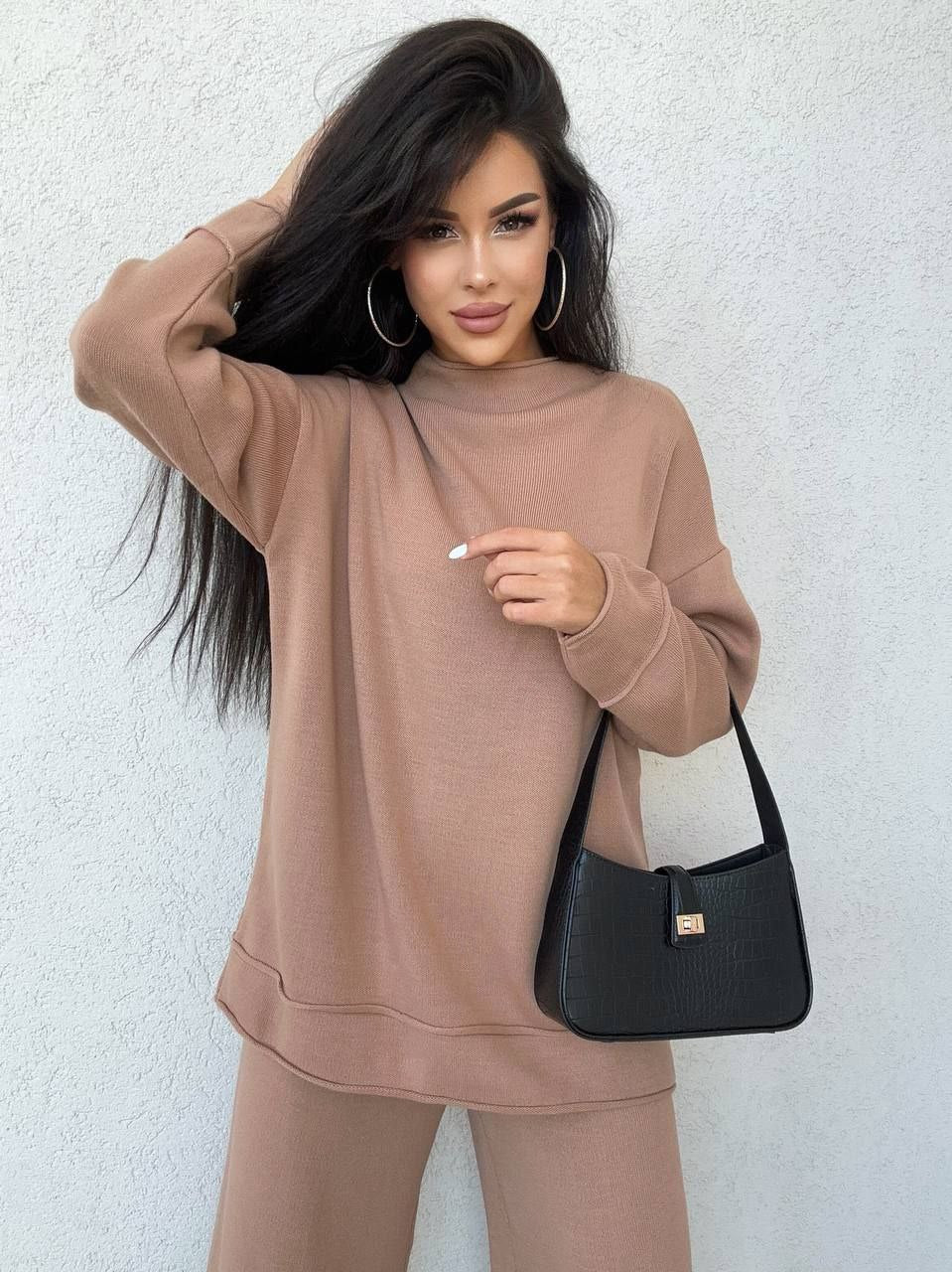 Woman wearing a brown outfit holding a black handbag against a light background