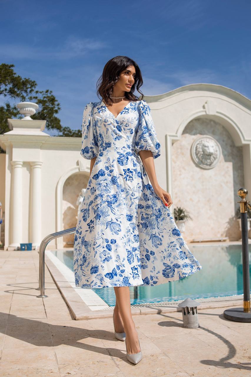 Woman in a blue floral dress standing in front of a classical building with a pool.