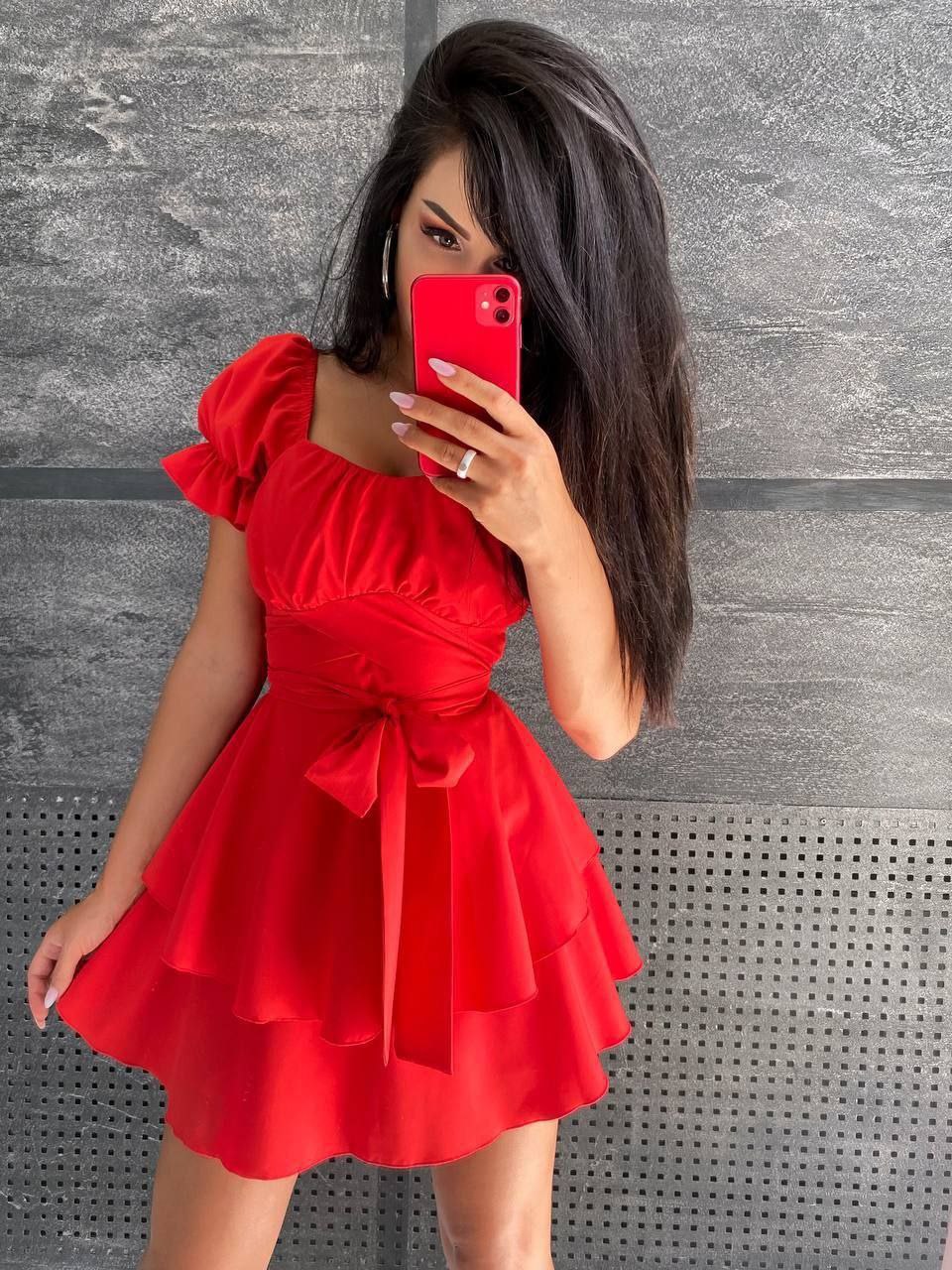 Woman in a red dress taking a selfie against a gray textured wall